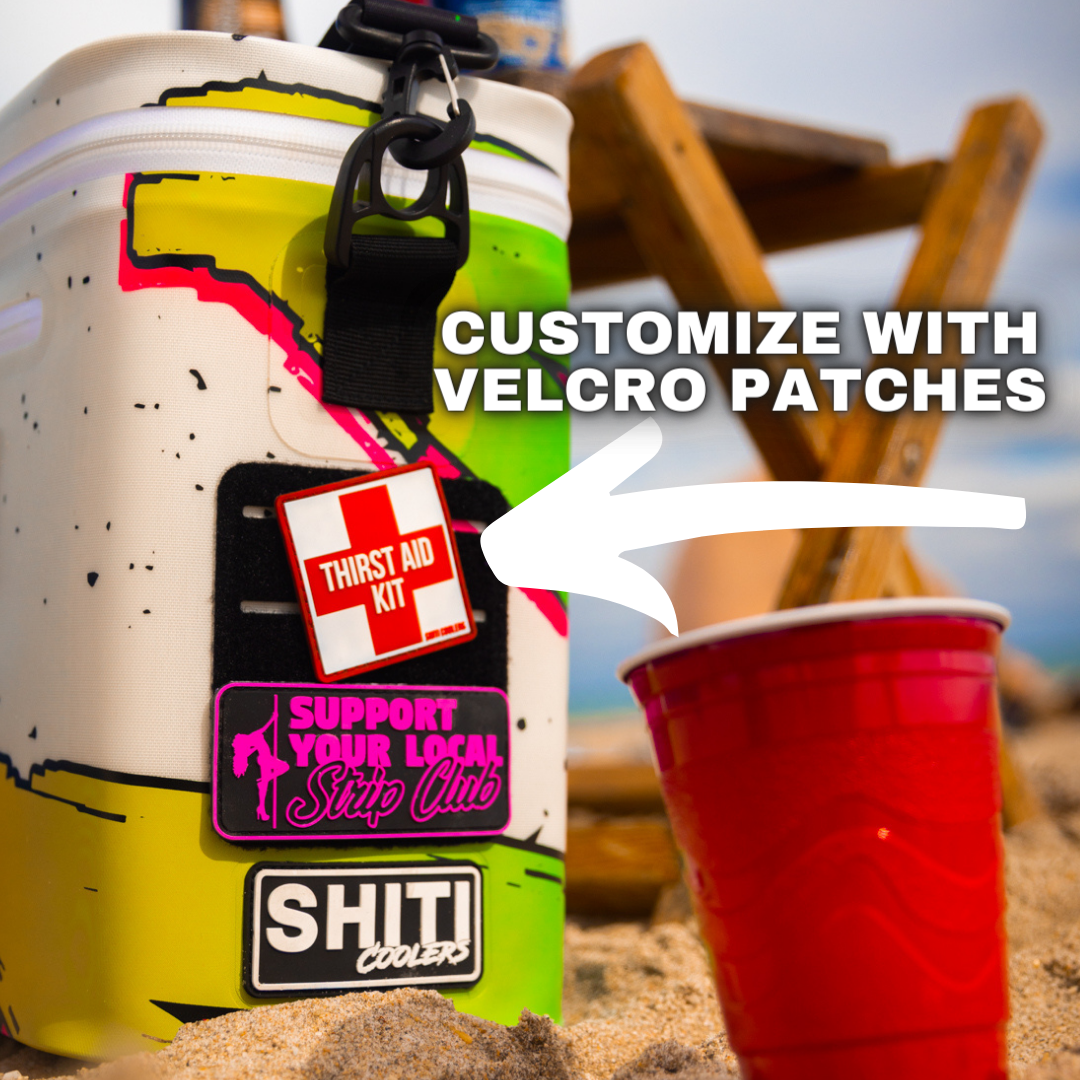 Boozer Soft Cooler in vibrant design with customizable Velcro patches, next to a red plastic cup on sandy beach.