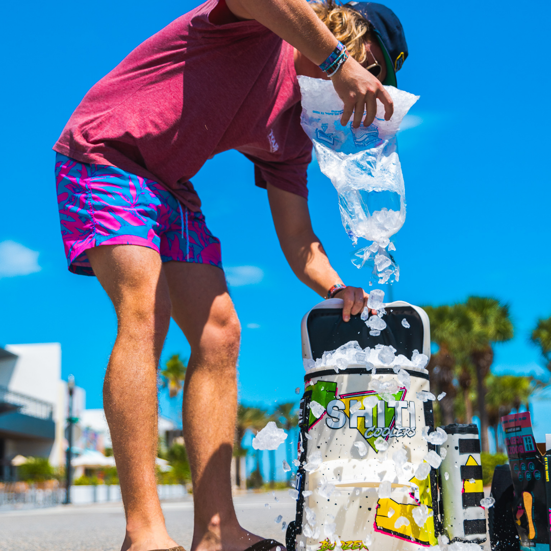 A person fills a Boozer Backpack Cooler with ice, showcasing its 15-can capacity and vibrant design, perfect for outdoor parties.