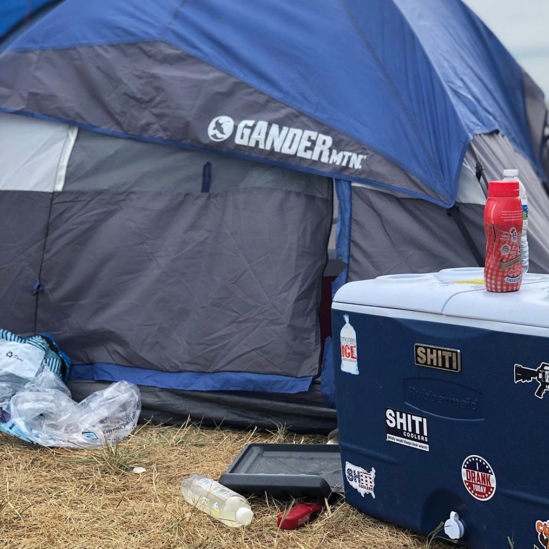 Chrome brand plate on a cooler beside a tent, surrounded by camping gear and outdoor debris.