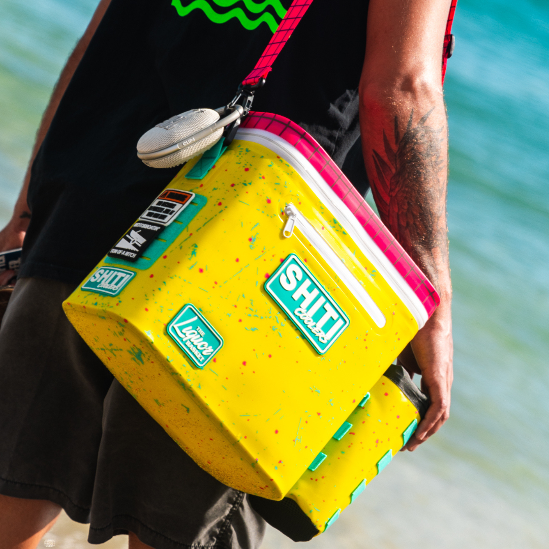 Bright yellow soft cooler designed to hold 12 cans, featuring colorful splatter design and adjustable strap, perfect for outdoor use.