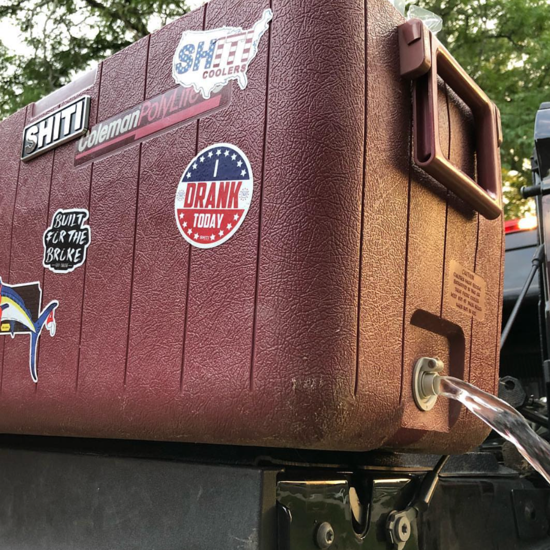 Close-up of a maroon cooler with stickers, featuring a chrome brand plate and a spout for easy pouring.