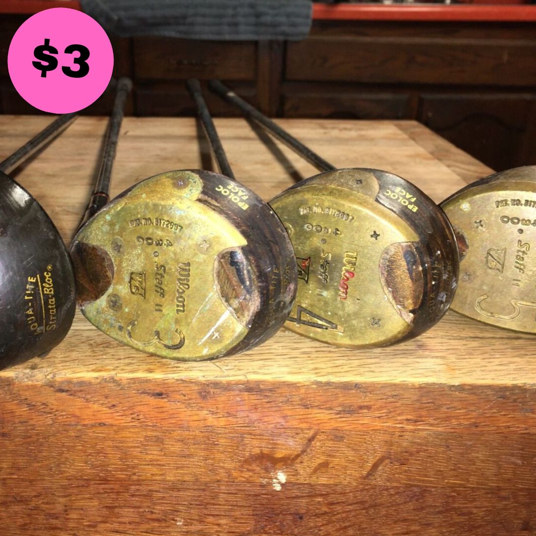 Gilmores Golf Set featuring three vintage golf clubs with worn brass heads, displayed on a wooden surface.