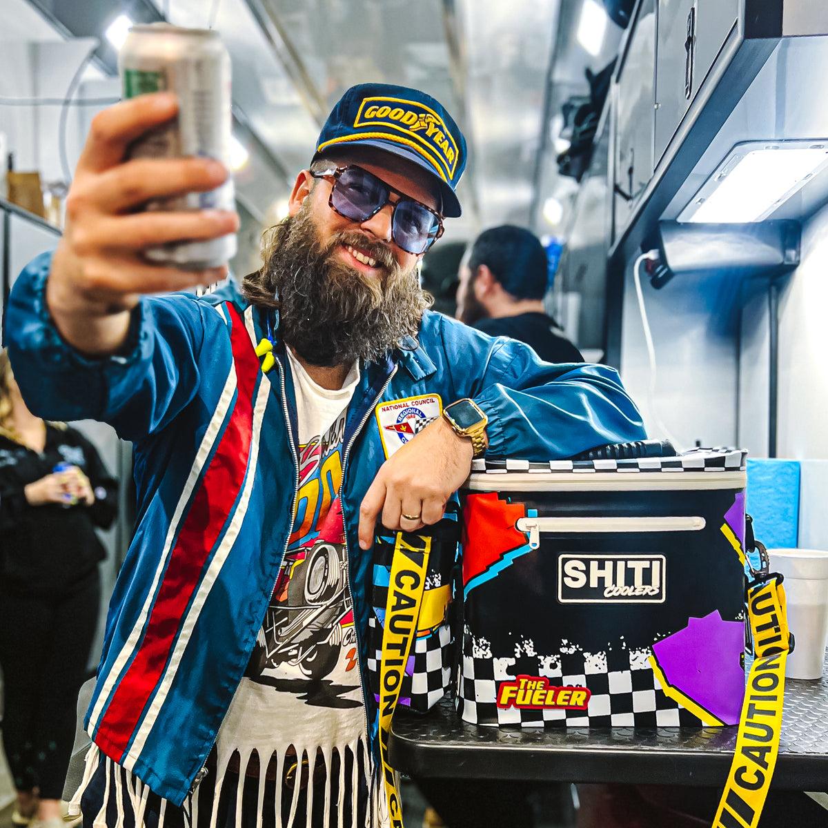 A man in sunglasses and a colorful jacket holds a can while posing next to the SHITI Coolers Fueler Soft Cooler.