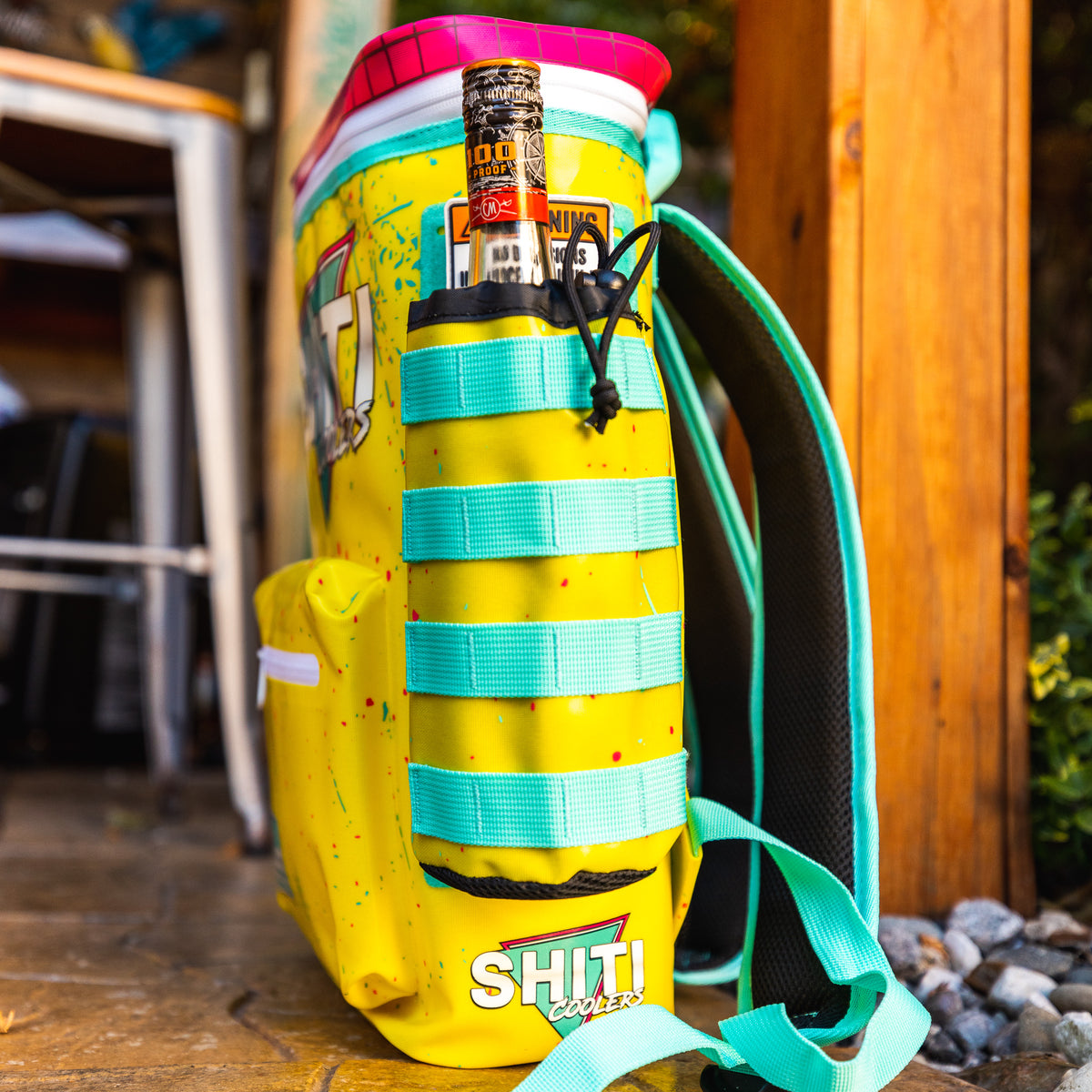 Bright yellow cooler with a liquor basket drink sleeve attachment, featuring a bottle secured in a colorful strap system.
